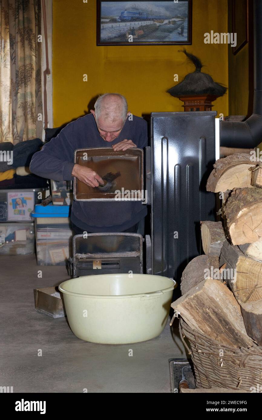 homme âgé mûr nettoyant le verre dans la porte sur le brûleur à bois domestique Banque D'Images