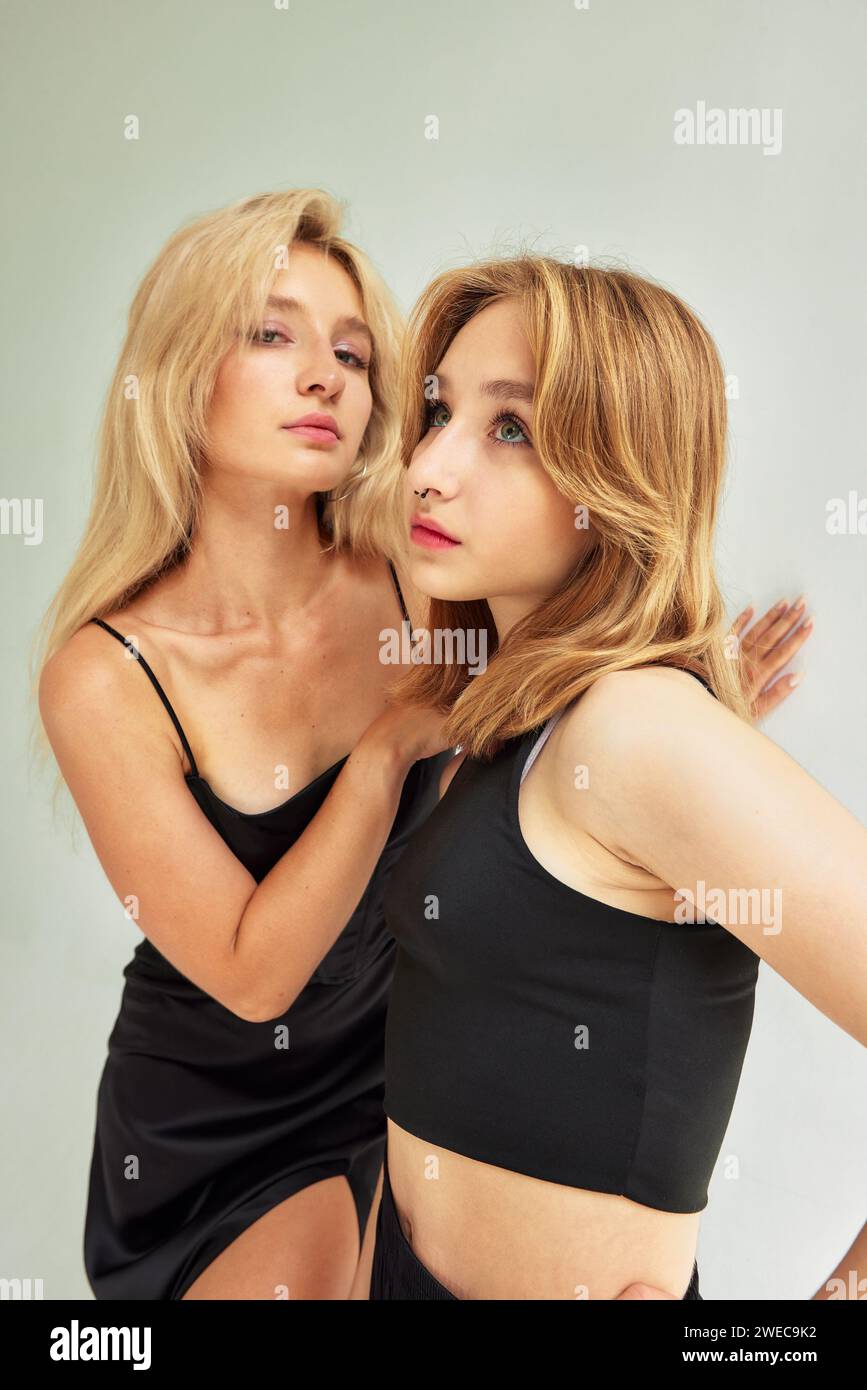 Portrait de studio demi-longueur de deux jeunes femmes sexy habillées de vêtements noirs sur fond blanc. Des filles blondes élégantes serrant doucement. Modèles glamour Banque D'Images