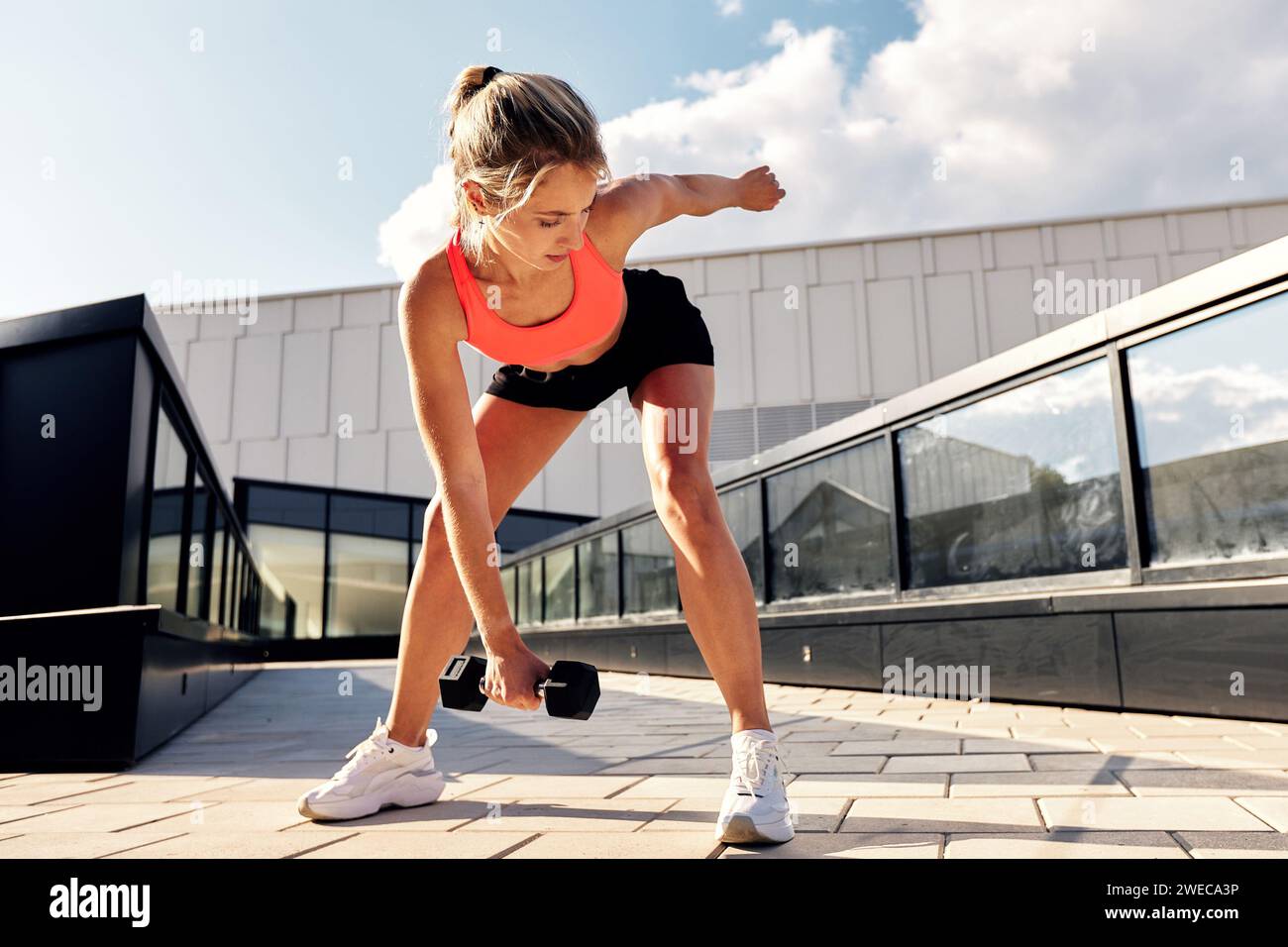 Femme athlétique en vêtements de sport faisant des squats avec des haltères dans la rue sur les escaliers de la ville, entraînement fonctionnel dans un environnement urbain, vie active Banque D'Images