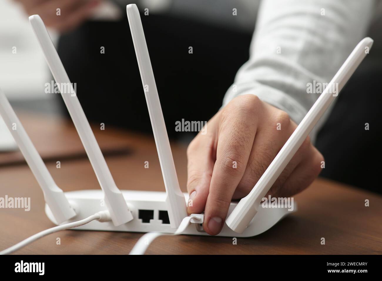 Homme insérant le câble dans le routeur Wi-Fi à la table en bois à l'intérieur, gros plan Banque D'Images