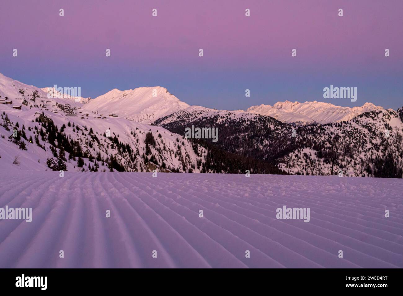 Montagnes enneigées au crépuscule avec un ciel violet et une piste de ski fraîchement soignée au premier plan, Belalp, Naters, Brig, Canton Valais, Suisse Banque D'Images