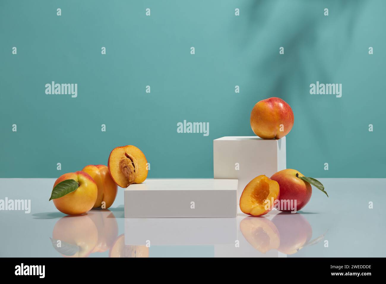 Deux podiums de forme géométrique placés sur la table miroir avec quelques pêches. Fond bleu. La pêche (Prunus persica) peut aider à soutenir la régulation de la glycémie Banque D'Images