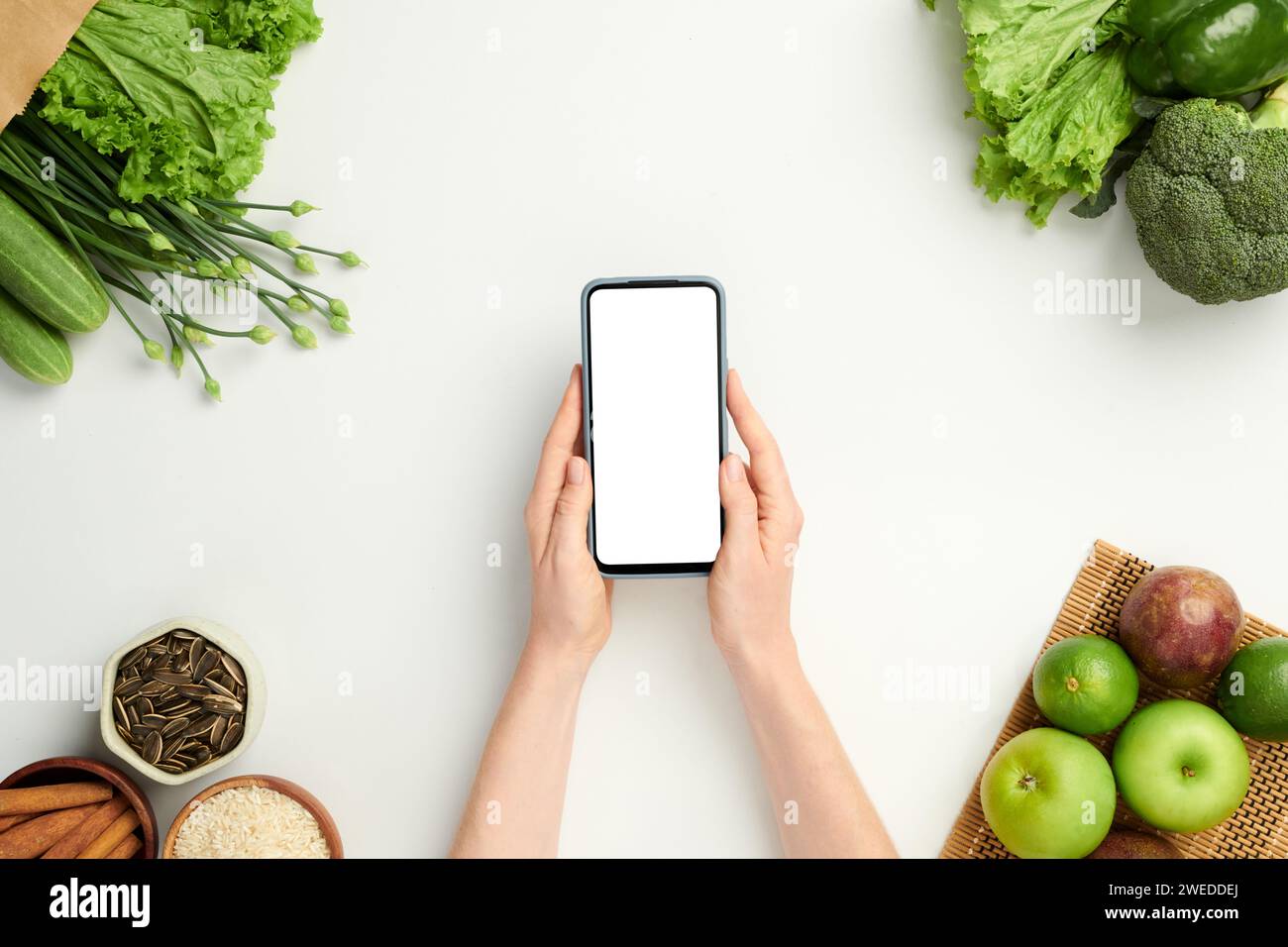 Mains de la personne tenant smartphone avec écran vide lors de la commande de fruits et légumes frais en ligne Banque D'Images
