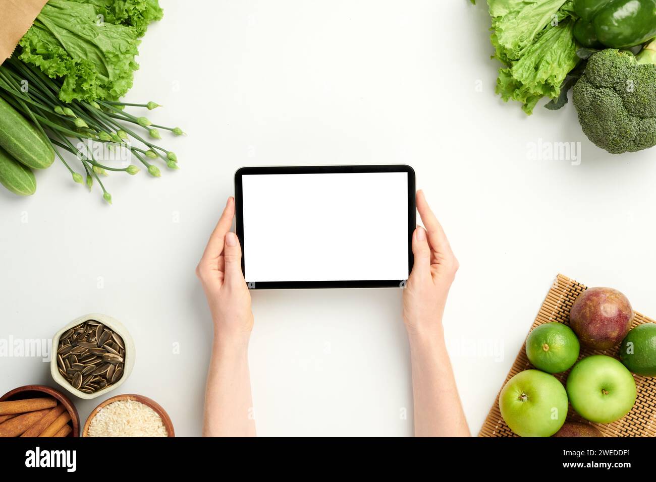 Mains de femme tenant la tablette ordinateur avec écran vide sur la table avec épicerie Banque D'Images