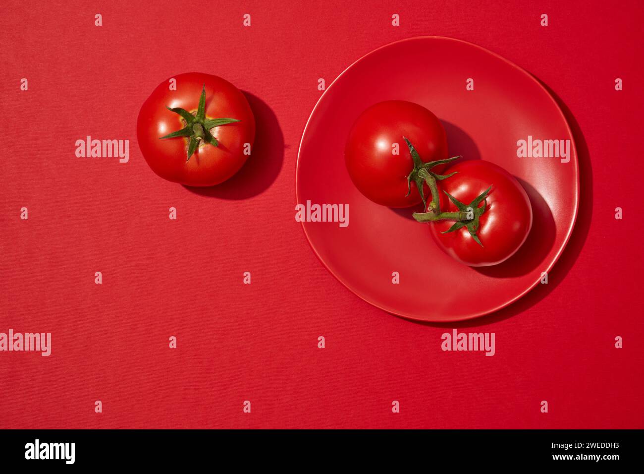 Sur un fond rouge, un plat avec des tomates est affiché. Espace vide pour la beauté présentation originale du produit de tomate (Solanum lycopersicum) extra Banque D'Images