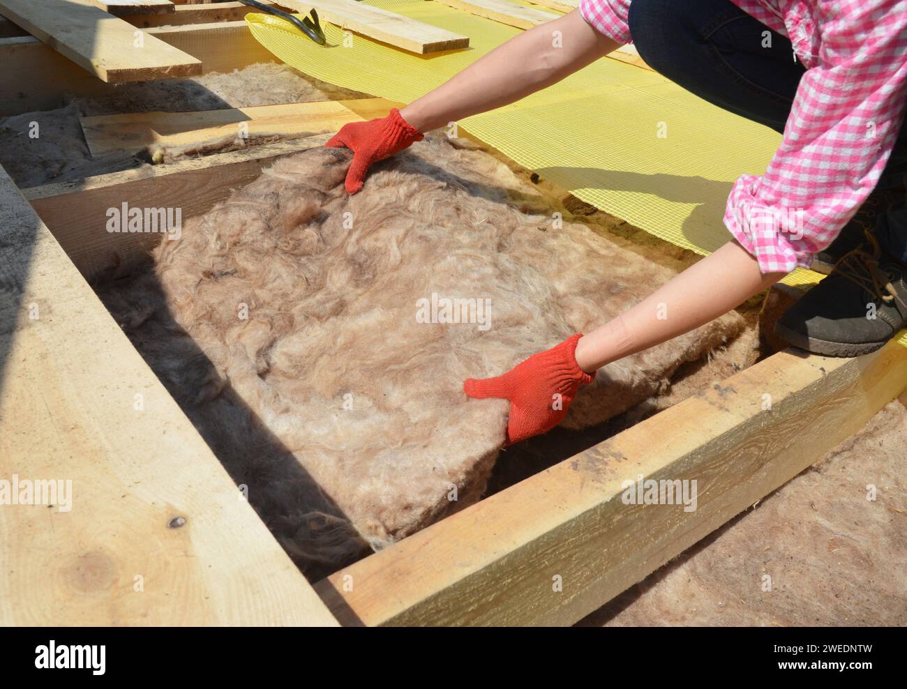 Bricolage dans la construction de toiture : une femme portant des gants de protection installe de la laine de verre, de la laine minérale ou une couverture d'isolation thermique sur le toit métallique Banque D'Images