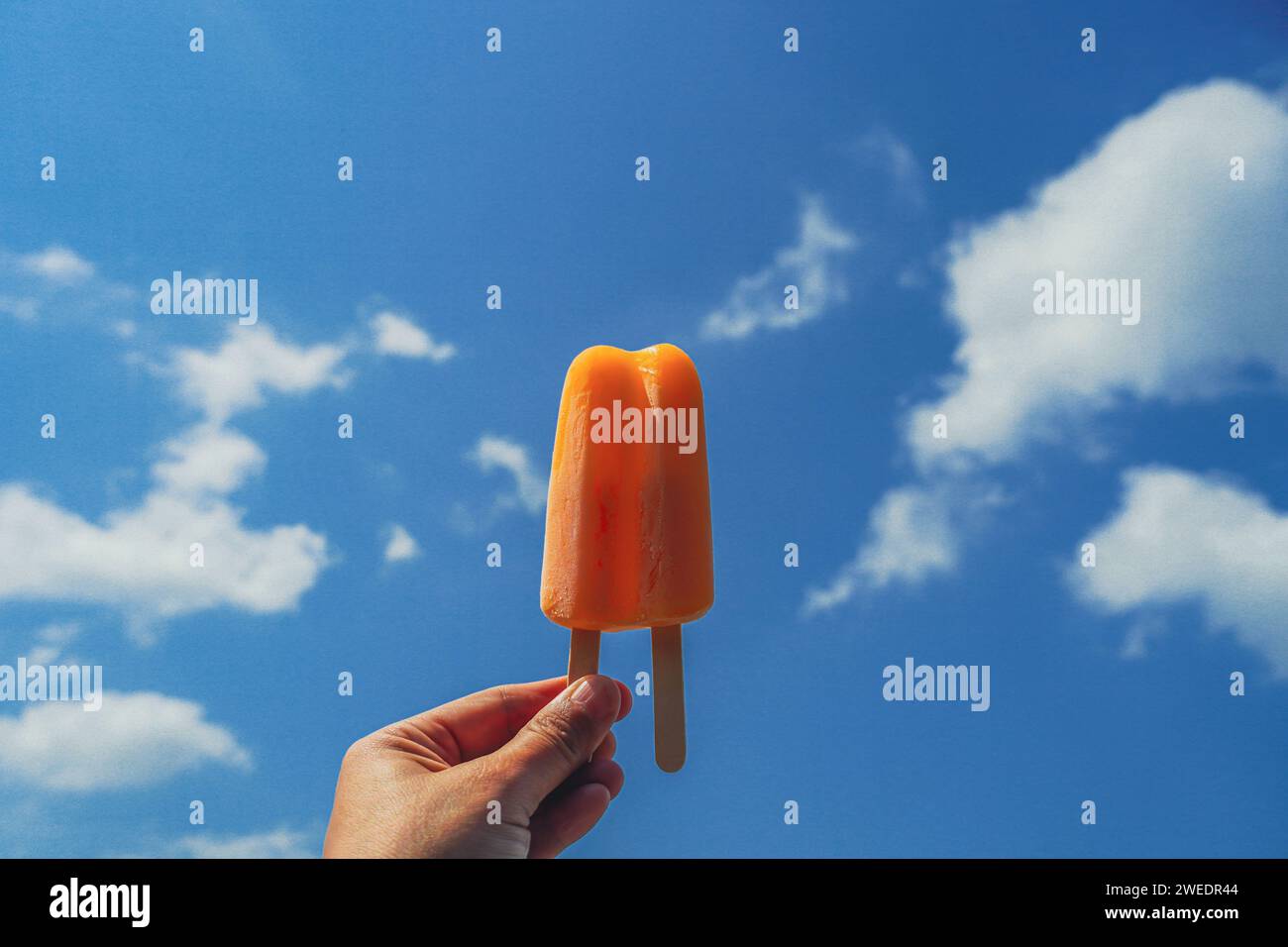 Glaces orange sur fond de ciel bleu. Popsicle orange dans la main de femme. Main féminine tenant le popsicle orange fondant sur un fond de ciel bleu dans le summe Banque D'Images