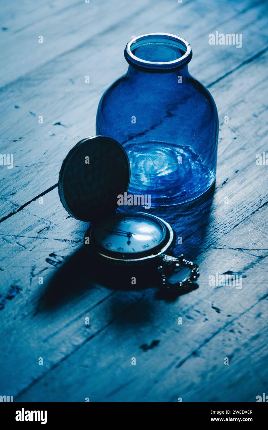 Montre de poche à côté d'une bouteille bleue vide Banque D'Images