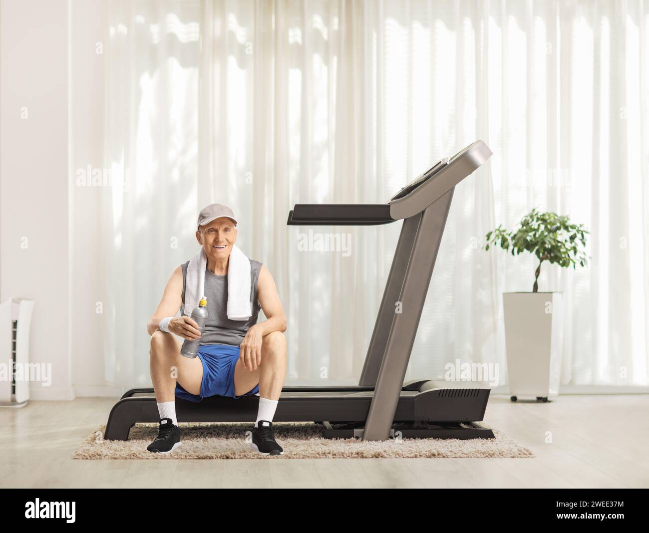 Homme âgé reposant sur un tapis roulant à la maison avec une bouteille d'eau Banque D'Images