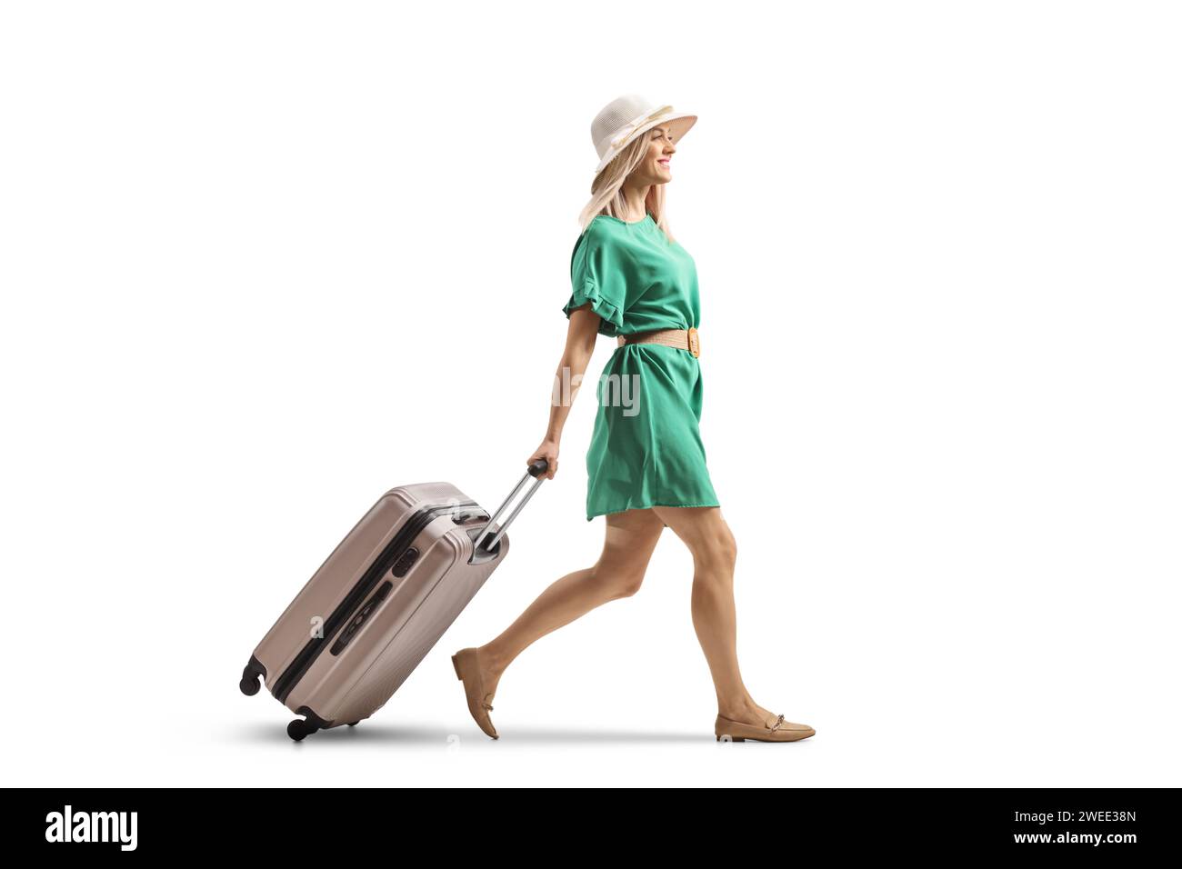 Jeune femme dans une robe verte marchant et tirant une valise isolée sur fond blanc Banque D'Images