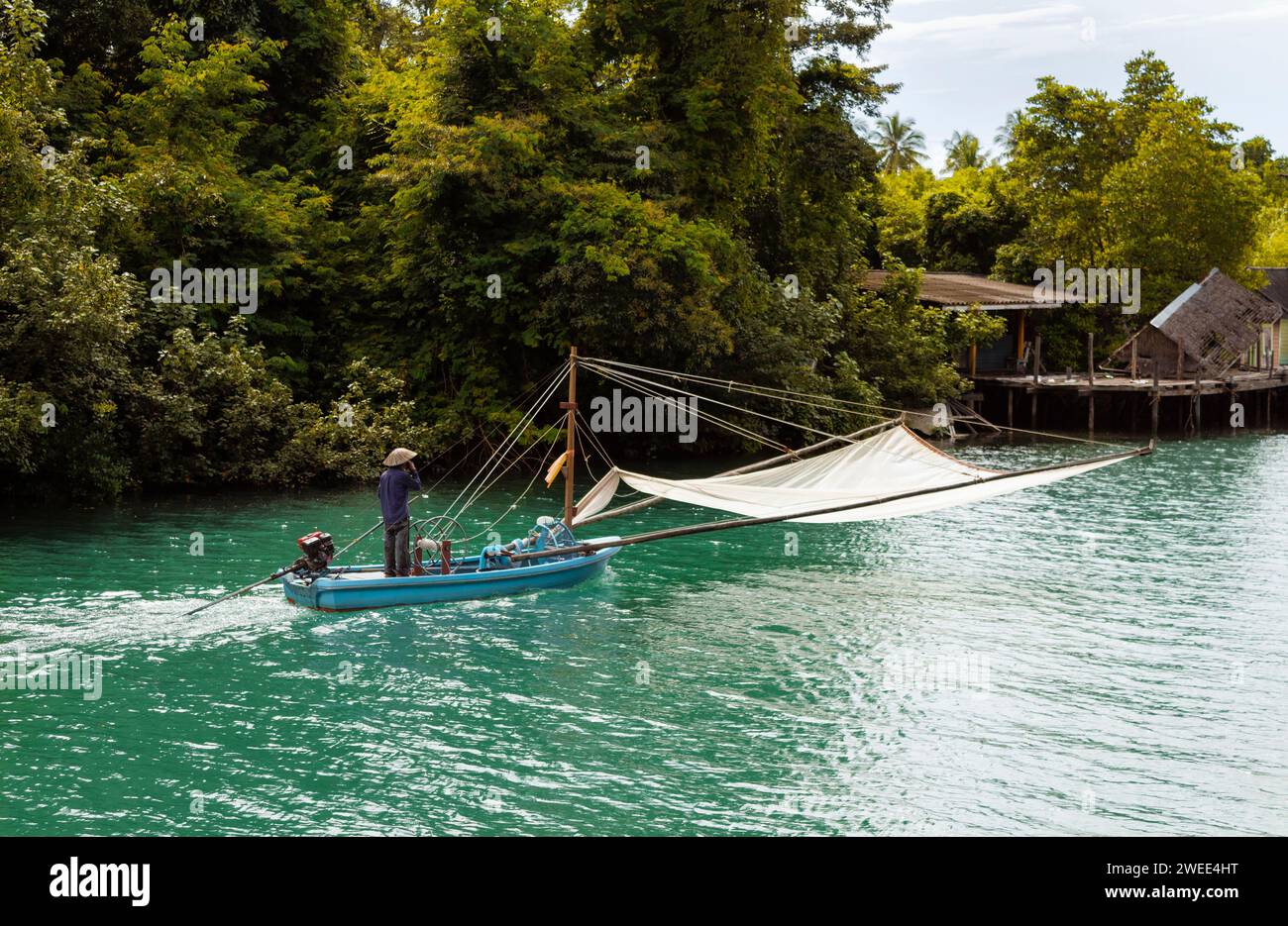 Un pêcheur asiatique dans un chapeau de cône flotte le long de la rivière sur un bateau de pêche motorisé avec un filet de pêche. Thaïlande, Koh Chang. Banque D'Images