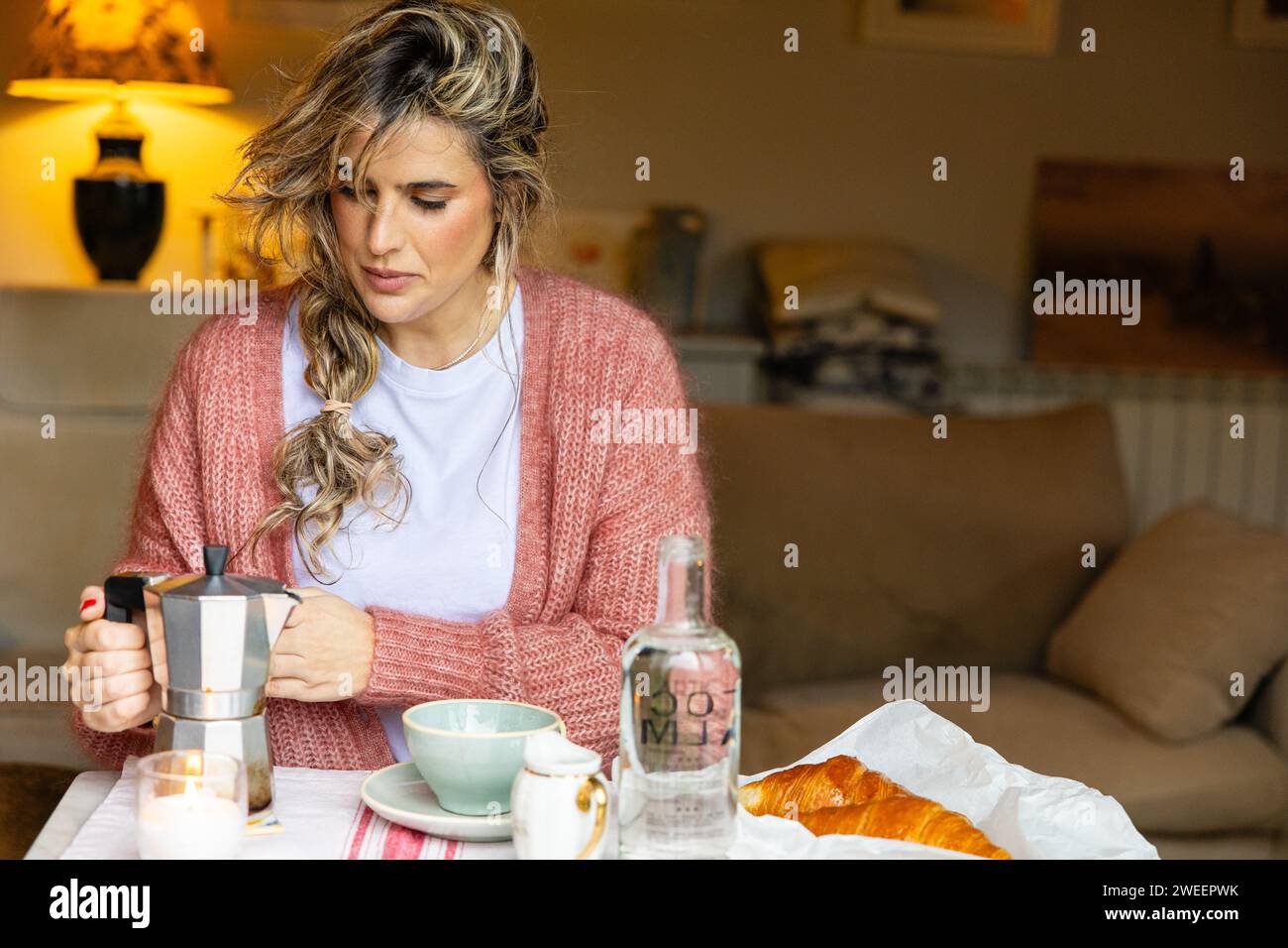 Un cadre de petit déjeuner intime avec une femme appréciant le plaisir simple de faire du café à l'aide d'un pot de moka, complété par un croissant frais. Banque D'Images