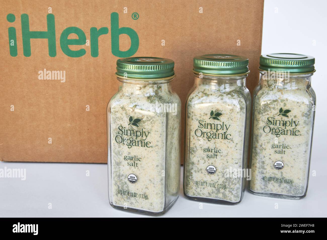 Trois pots de sel d'ail et d'herbes de marque Simply Organic, assaisonnement d'épices. Boîte en carton avec logo iHerb, achats en ligne. Acheter des produits dans un onli Banque D'Images
