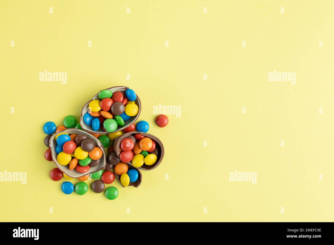 Vue de dessus des bonbons multicolores dispersés dans les oeufs de Pâques en chocolat cassé sur fond jaune Banque D'Images