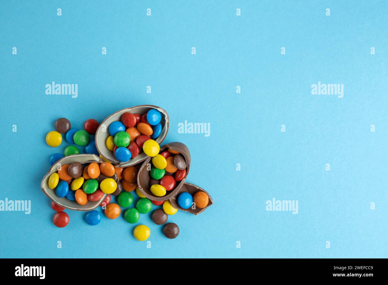 Vue de dessus des bonbons multicolores dispersés dans les oeufs de Pâques en chocolat cassé sur fond bleu Banque D'Images