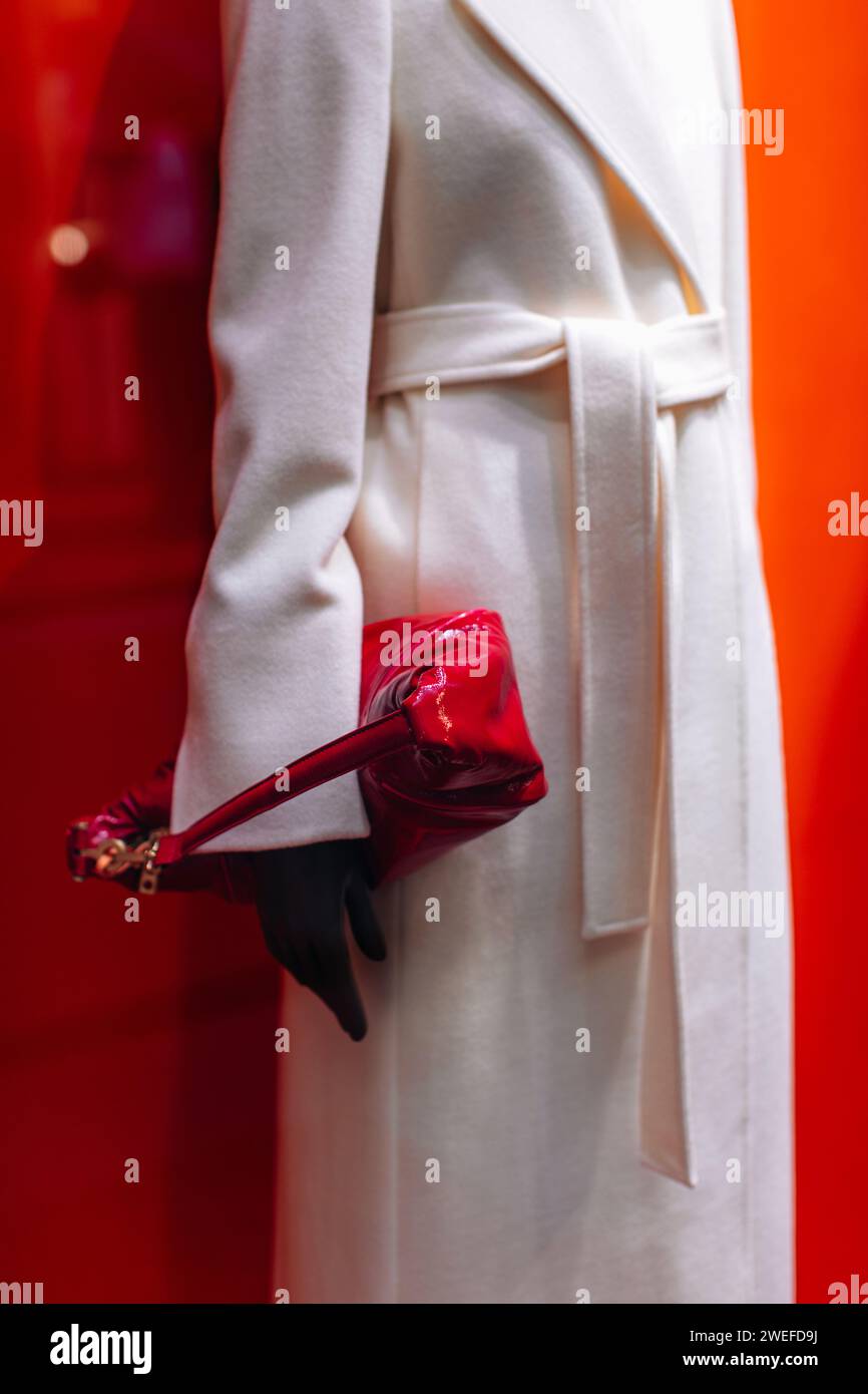 Détails fantaisie d'un manteau long blanc classique avec une ceinture et un sac à main rouge verni. Vêtements et accessoires de mode pour femmes Banque D'Images