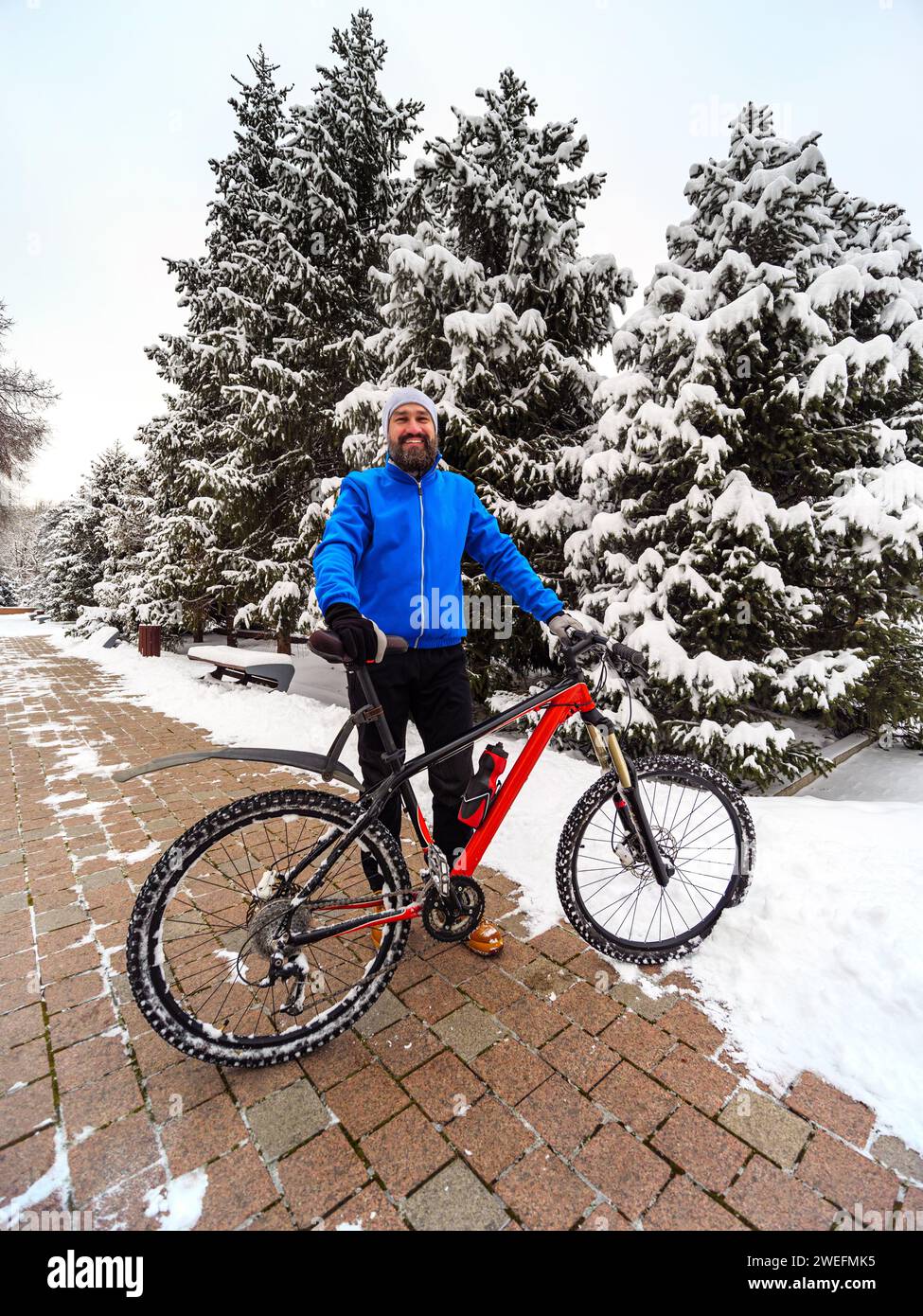 Homme barbu heureux avec un vélo dans un parc d'hiver de la ville. Mode de vie actif et sain en ville Banque D'Images