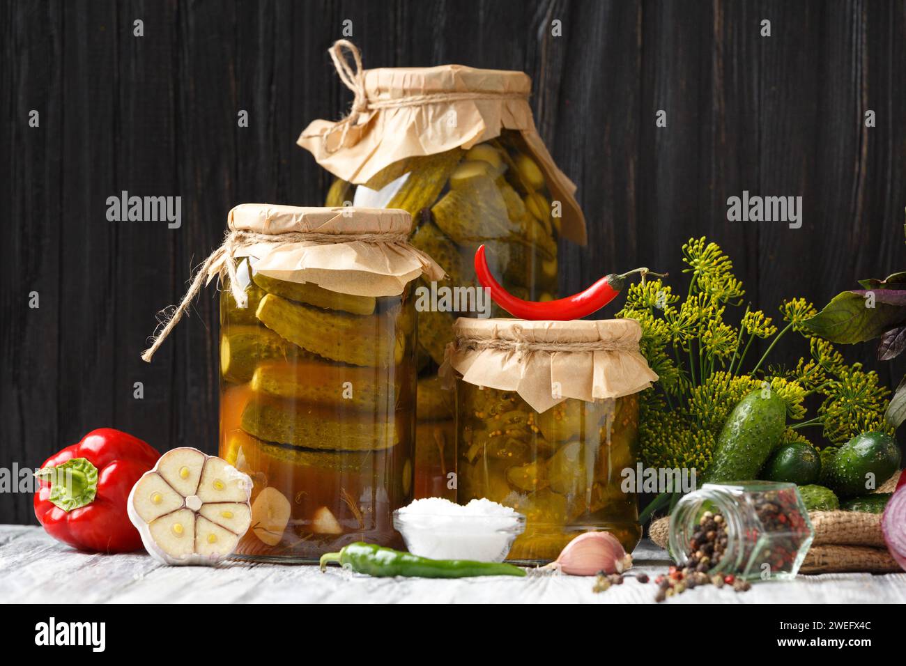 Concombres en conserve dans des bocaux fermés, cornichons frais, légumes et épices pour marinade sur fond en bois. Banque D'Images