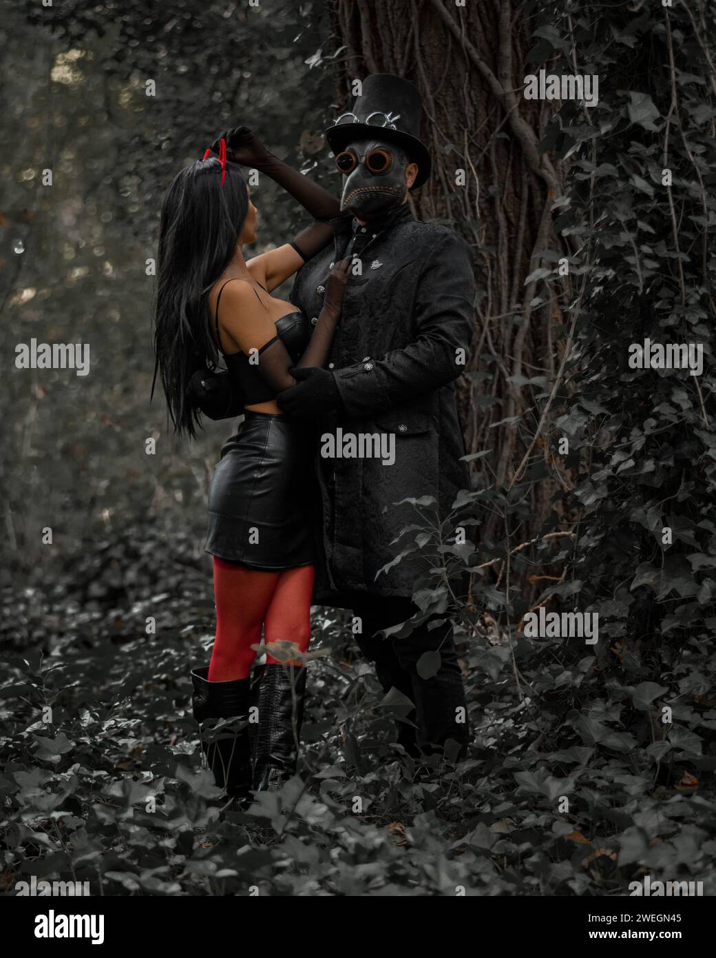 Un homme dans un chapeau haut de forme et un masque debout aux côtés d'une femme élégante avec des cornes de diable dans une forêt Banque D'Images