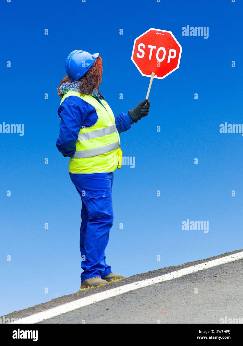 Femme en gilet de signalisation jaune et casque de sécurité bleu se tient sur le côté de la route tenant un panneau d'arrêt Banque D'Images