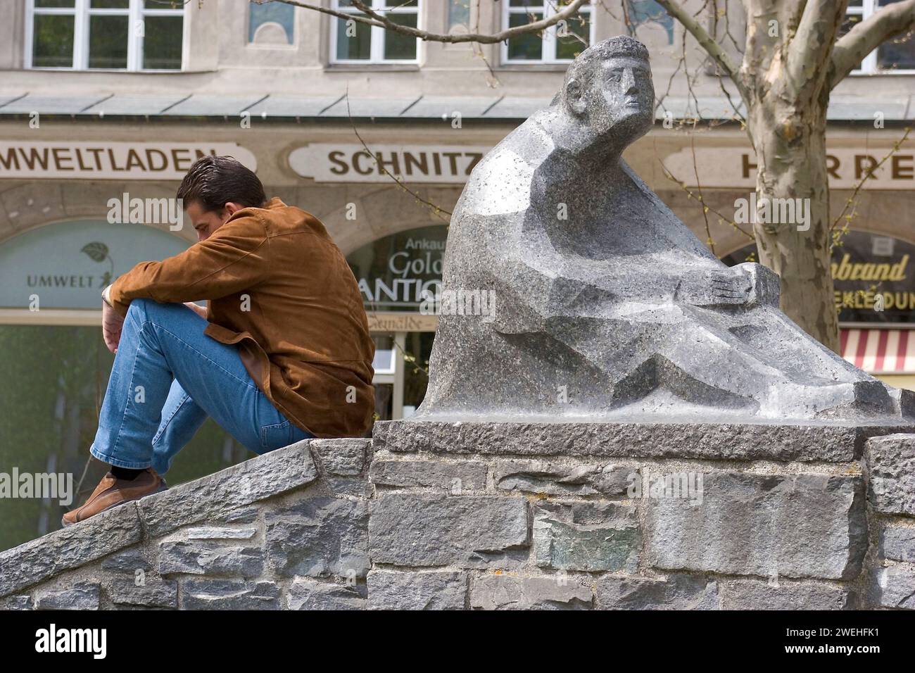 Un homme assis exactement dans la même position qu'un personnage de pierre à côté de lui, Rindermarktbrunnen, Munich, Bavière, Allemagne, Europe Banque D'Images