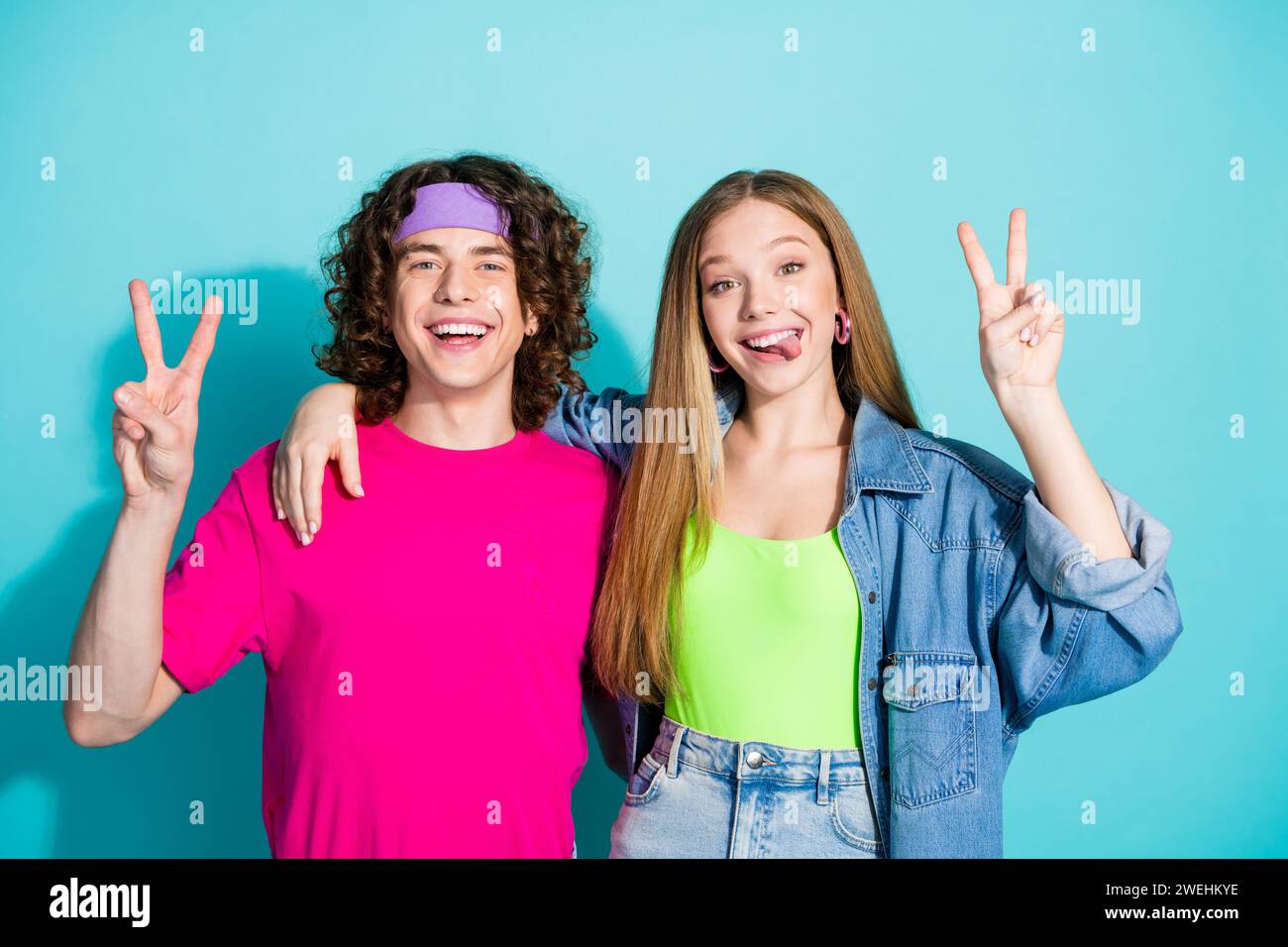 Portrait de deux amis adolescents montrant la langue de bâton de signe double v posant à la fête hippie isolé sur fond de couleur aigue-marine Banque D'Images