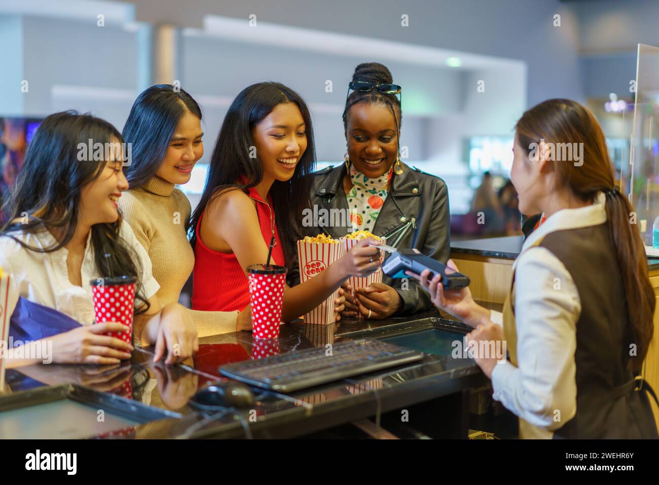 Divers groupes d'amies féminines, représentant différentes nationalités, utilisent joyeusement les cartes de crédit pour payer les billets de cinéma au théâtre Banque D'Images