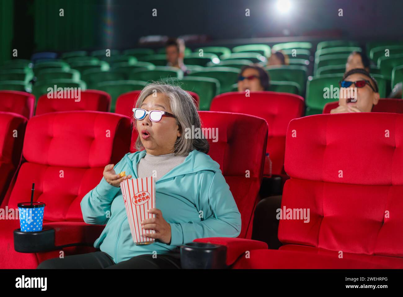 Femme asiatique âgée comme elle exprime un véritable étonnement tout en regardant un film d'horreur au cinéma Banque D'Images