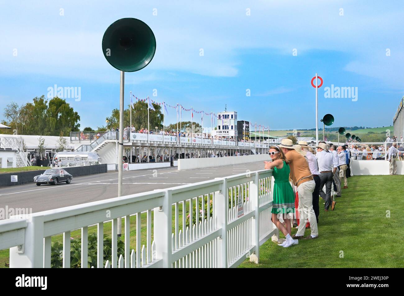 Spectateurs sur le circuit de course automobile Goodwood Revival. Jeune femme en robe verte plissée, lunettes de soleil blanches et bandeau typique de la mode rétro. Banque D'Images
