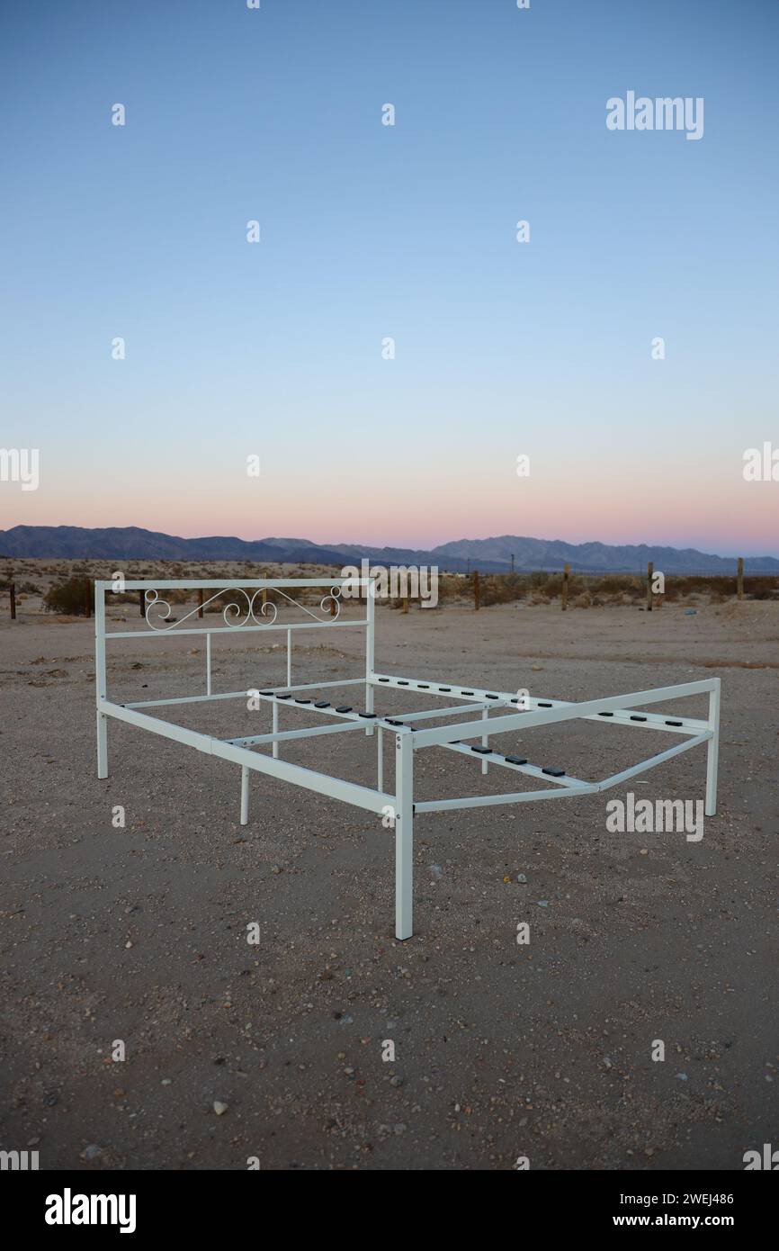 Cadre de lit abandonné au milieu du désert près de Joshua Tree, CA avec le coucher de soleil en arrière-plan. Banque D'Images