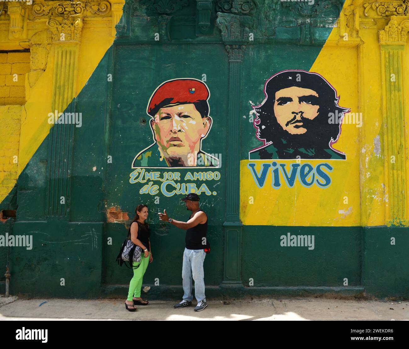 Un couple cubain socialisant devant un bâtiment peint avec les portraits de Hugo Chávez et Che Guevara dans la vieille Havane, Cuba. Banque D'Images