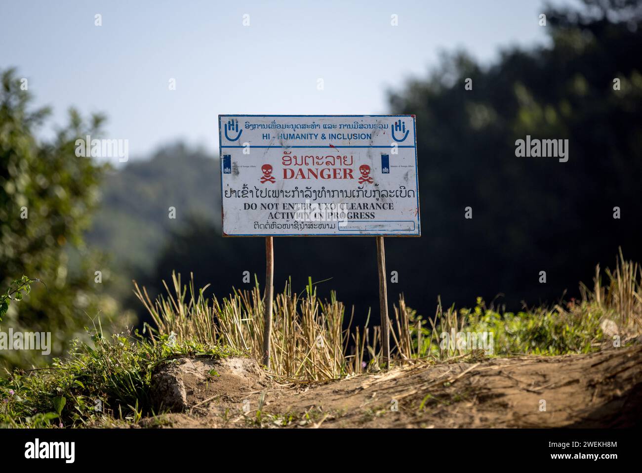 Un panneau « danger » se dresse près de Muang Mai, Laos, le 25 octobre 2023, à côté d’un riz paddy jonché d’une ordonnance non explosée (UXO) qui restent enterrés dans le sol après la campagne de bombardement des États-Unis pendant la guerre du Vietnam. Le site est nettoyé par des opérateurs de terrain ou des démineurs travaillant pour l'organisation non gouvernementale internationale humanité et inclusion. Banque D'Images