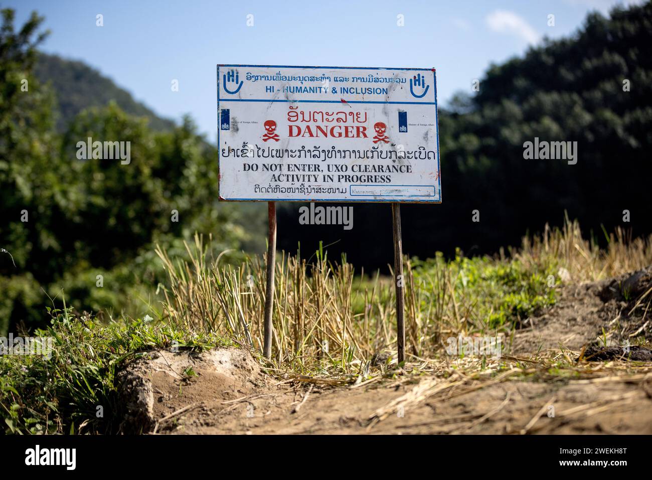 Un panneau « danger » se dresse près de Muang Mai, Laos, le 25 octobre 2023, à côté d’un riz paddy jonché d’une ordonnance non explosée (UXO) qui restent enterrés dans le sol après la campagne de bombardement des États-Unis pendant la guerre du Vietnam. Le site est nettoyé par des opérateurs de terrain ou des démineurs travaillant pour l'organisation non gouvernementale internationale humanité et inclusion. Banque D'Images