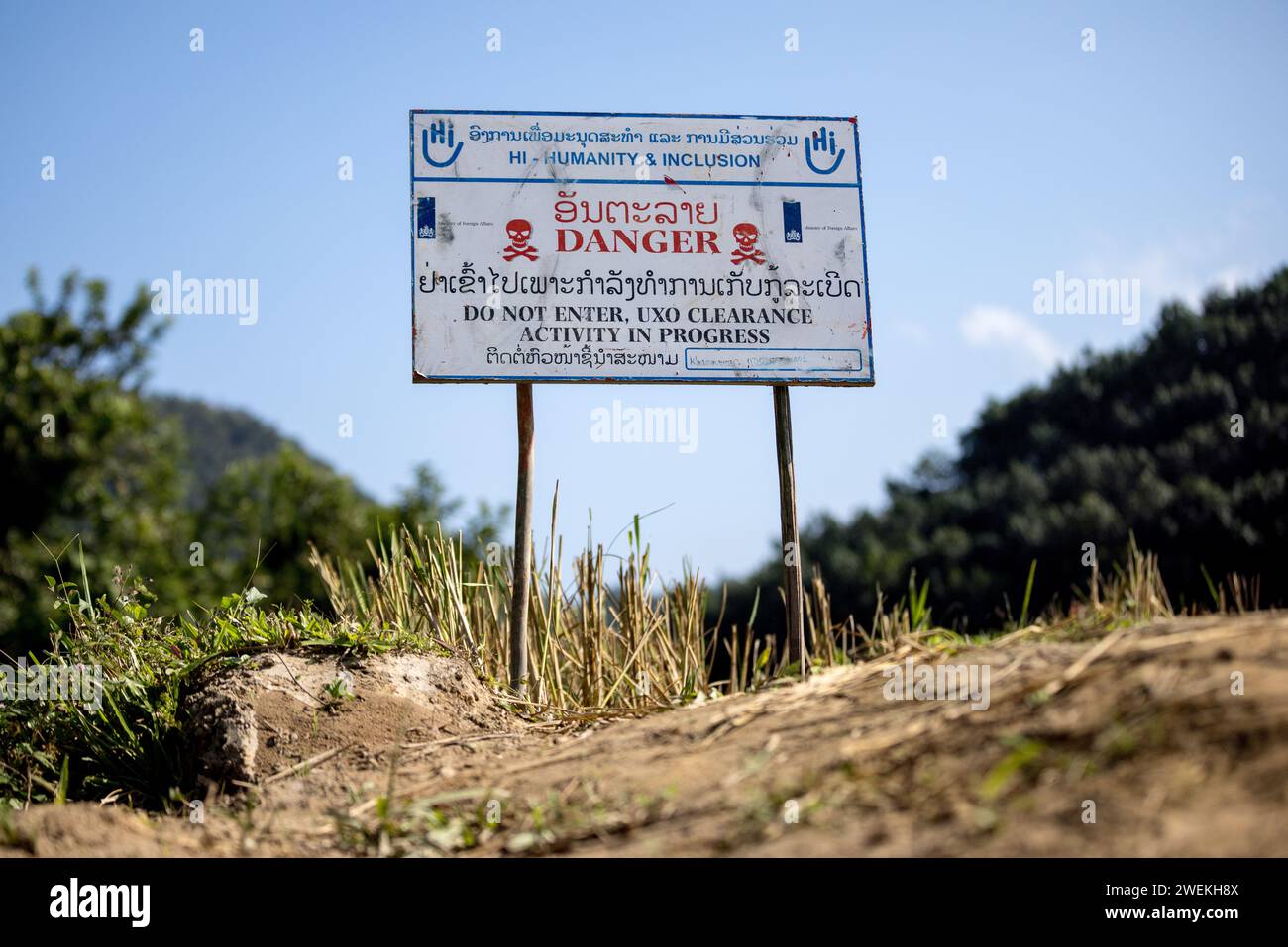 Un panneau « danger » se dresse près de Muang Mai, Laos, le 25 octobre 2023, à côté d’un riz paddy jonché d’une ordonnance non explosée (UXO) qui restent enterrés dans le sol après la campagne de bombardement des États-Unis pendant la guerre du Vietnam. Le site est nettoyé par des opérateurs de terrain ou des démineurs travaillant pour l'organisation non gouvernementale internationale humanité et inclusion. Banque D'Images