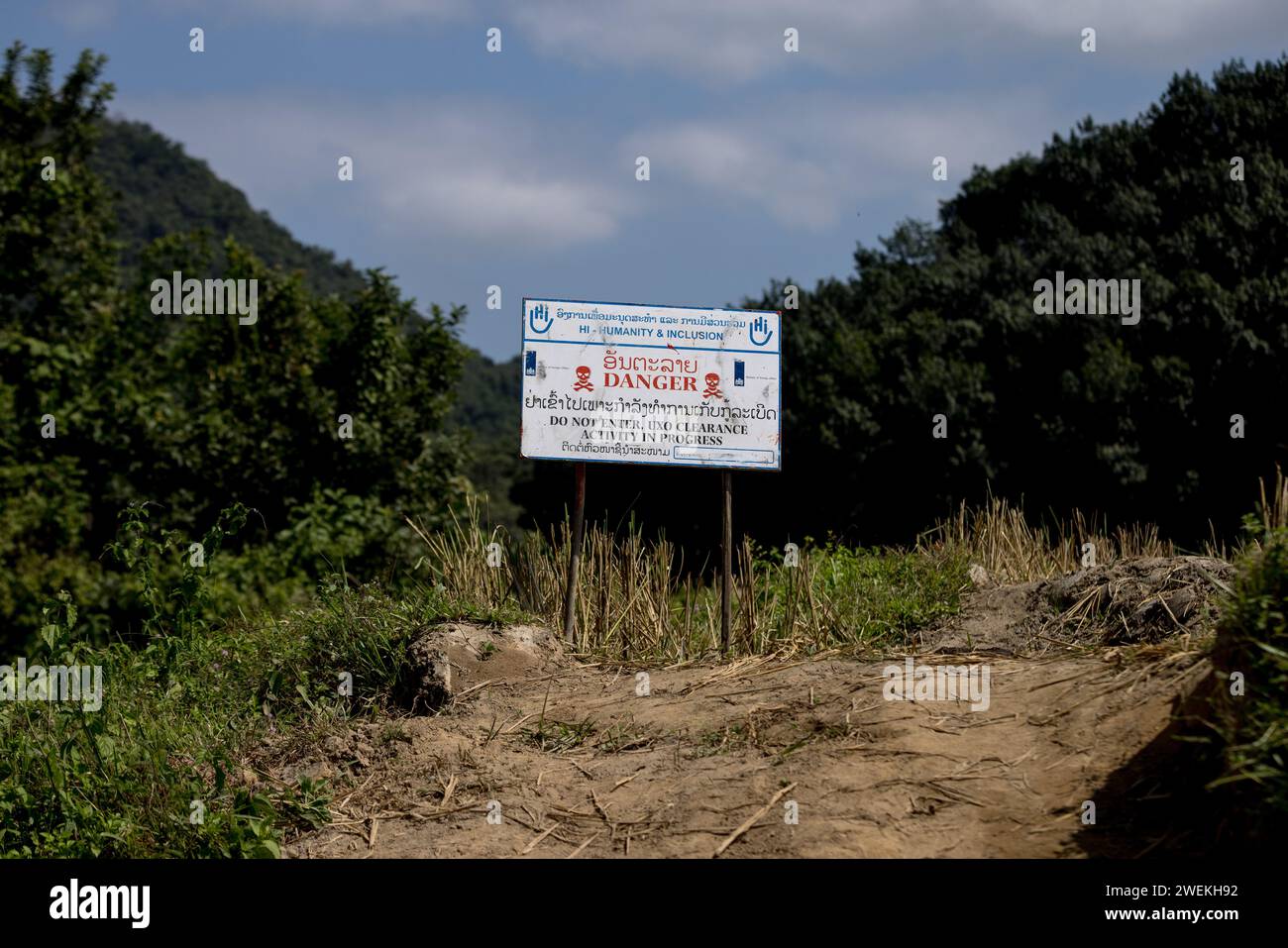 Un panneau « danger » se dresse près de Muang Mai, Laos, le 25 octobre 2023, à côté d’un riz paddy jonché d’une ordonnance non explosée (UXO) qui restent enterrés dans le sol après la campagne de bombardement des États-Unis pendant la guerre du Vietnam. Le site est nettoyé par des opérateurs de terrain ou des démineurs travaillant pour l'organisation non gouvernementale internationale humanité et inclusion. Banque D'Images