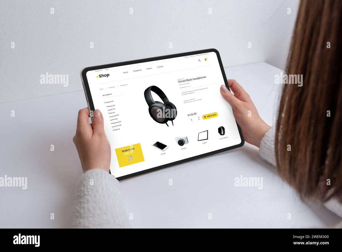 Girl achète en ligne des écouteurs, des gadgets et des appareils sur une page Web moderne de commerce électronique à l'aide d'une tablette. Navigation technologique transparente pour les appareils les plus récents Banque D'Images