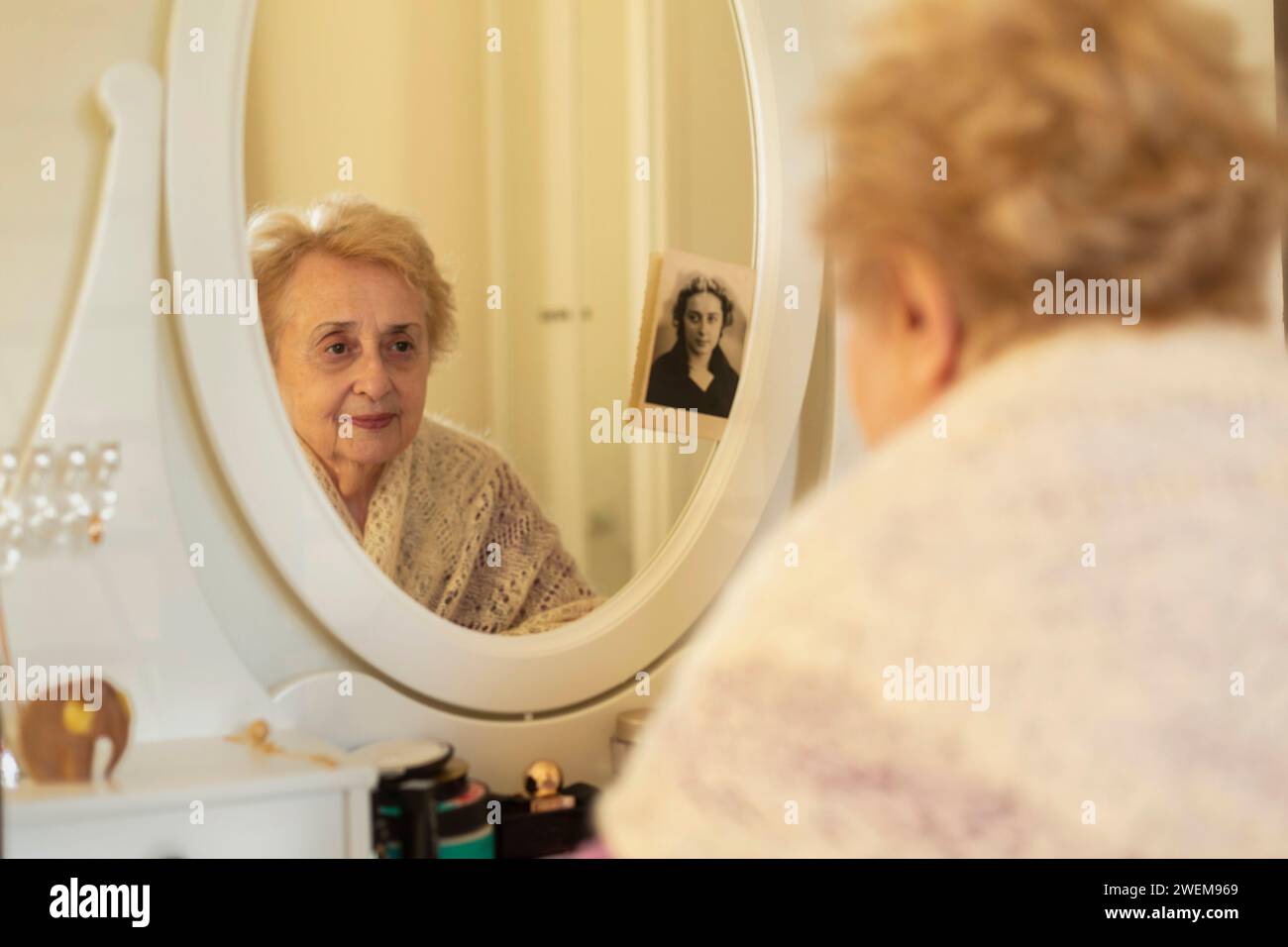 Femme âgée souriante regardant le reflet dans le miroir à côté de la vieille photo Banque D'Images