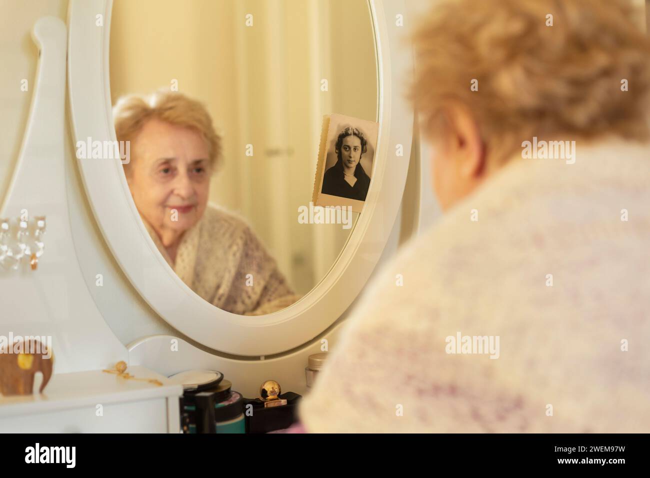 Femme âgée souriante regardant le reflet dans le miroir à côté de la vieille photographie Banque D'Images