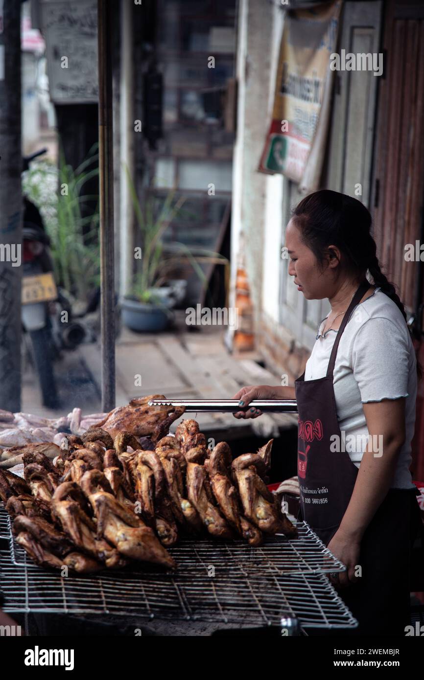 Femme laotienne grillant du poulet sur barbecue de rue Banque D'Images