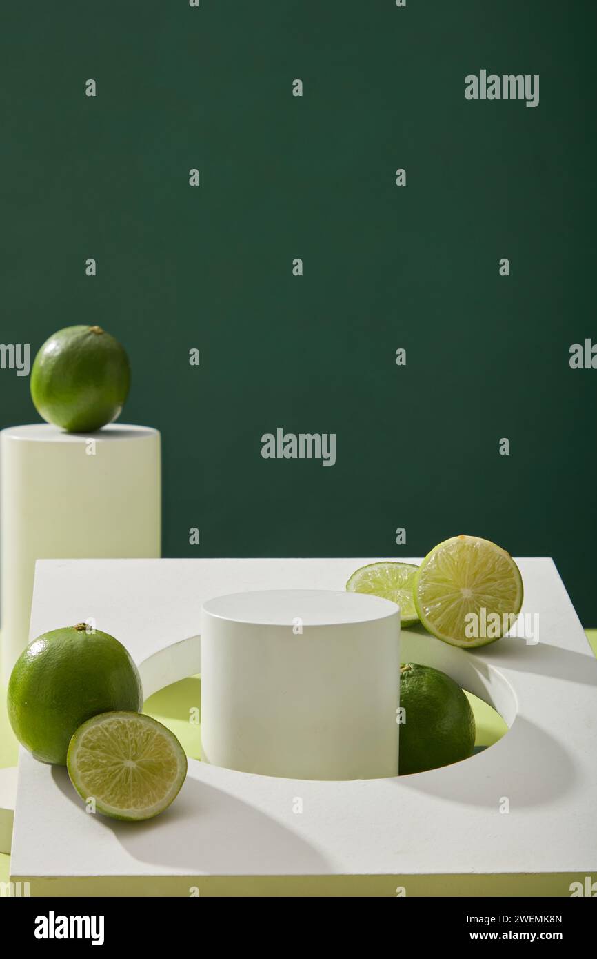 Fond minimal vierge avec podium vide blanc, objet géométrique et limes fraîches (Citrus aurantifolia) décorées sur fond sombre. Espace pour produ Banque D'Images