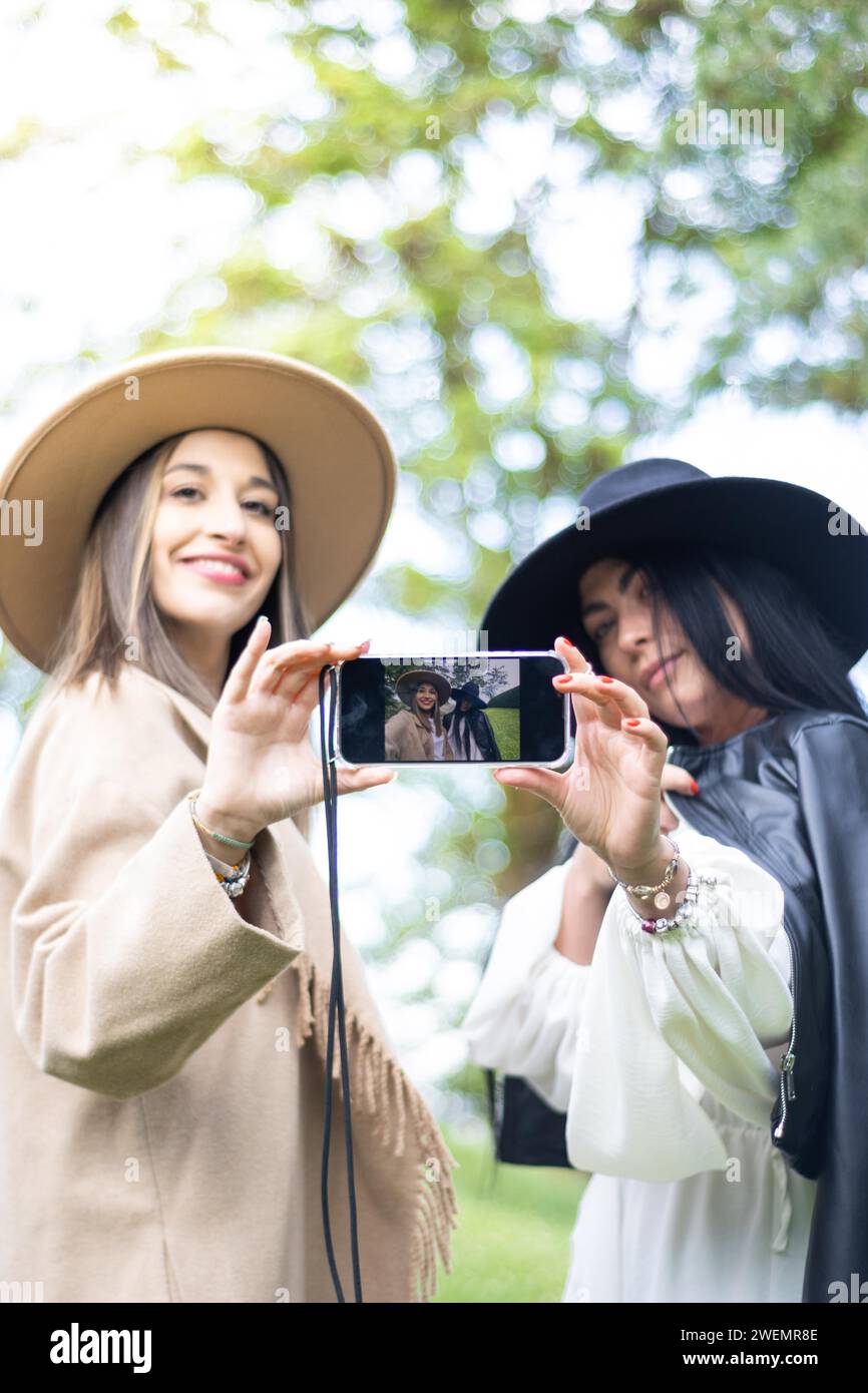 Vue frontale verticale de deux amis élégants saisissant tous les deux un téléphone portable pour prendre un selfie Banque D'Images