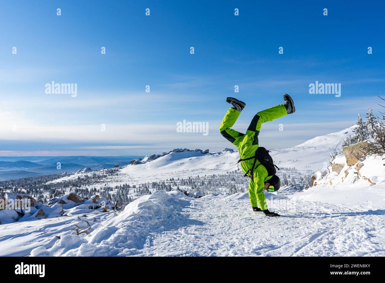 L'homme se tient sur ses mains à l'envers tenue vert acide brillant : costume chaud, lunettes, casque noir. Fond de montagnes enneigées à la station de ski de Sheregesh. CA Banque D'Images