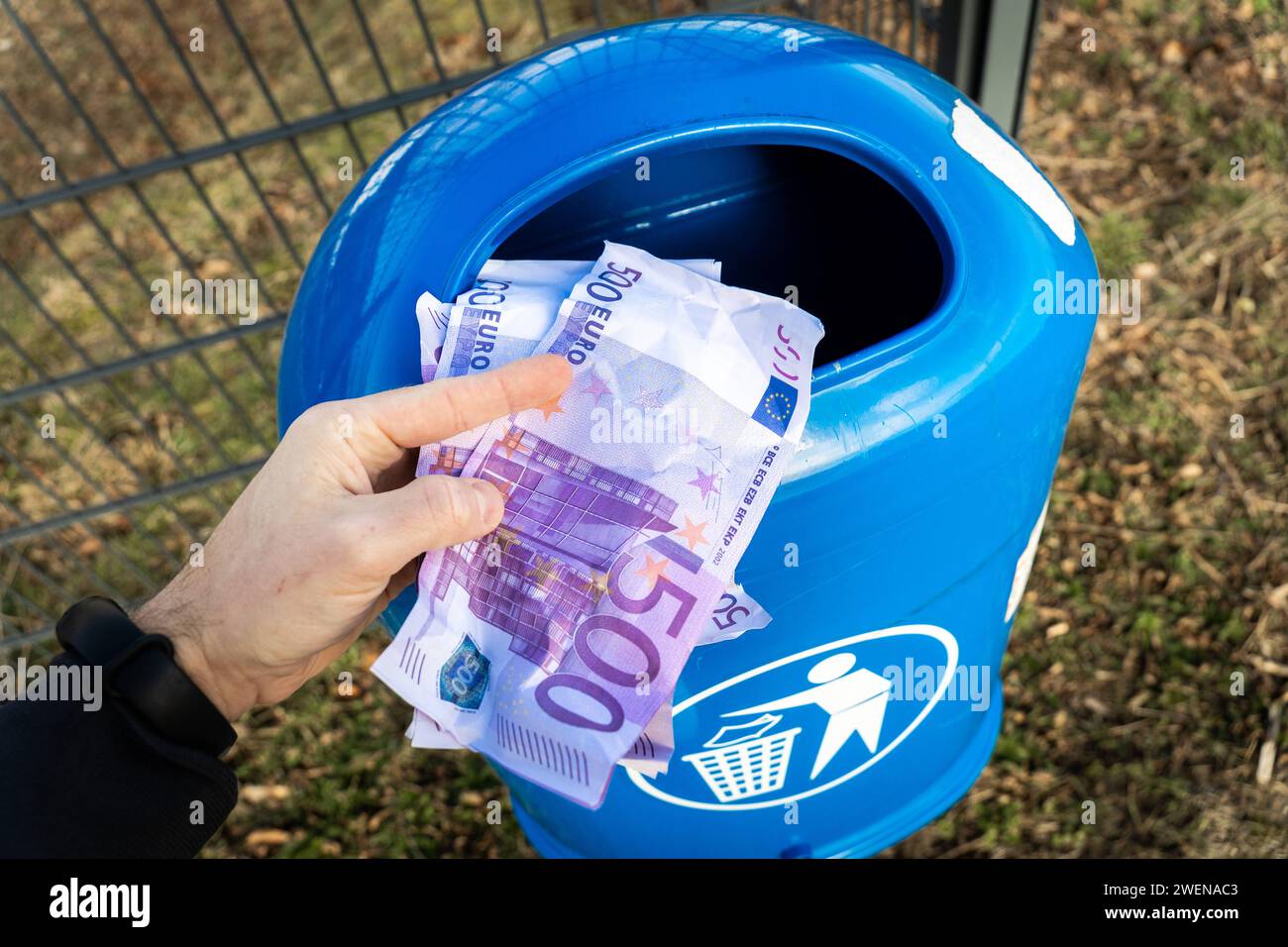 Langweid, Bavière, Allemagne - 26 janvier 2024 : un homme jette des billets de banque en euros dans une poubelle bleue. Image symbolique de la perte de valeur de l'argent, de la récession et de l'inflation *** Mann wirft Euro Bargeld Geldscheine in einen blauen Mülleimer. Symbolbild Wertverlust von Geld, Rezession und inflation Banque D'Images