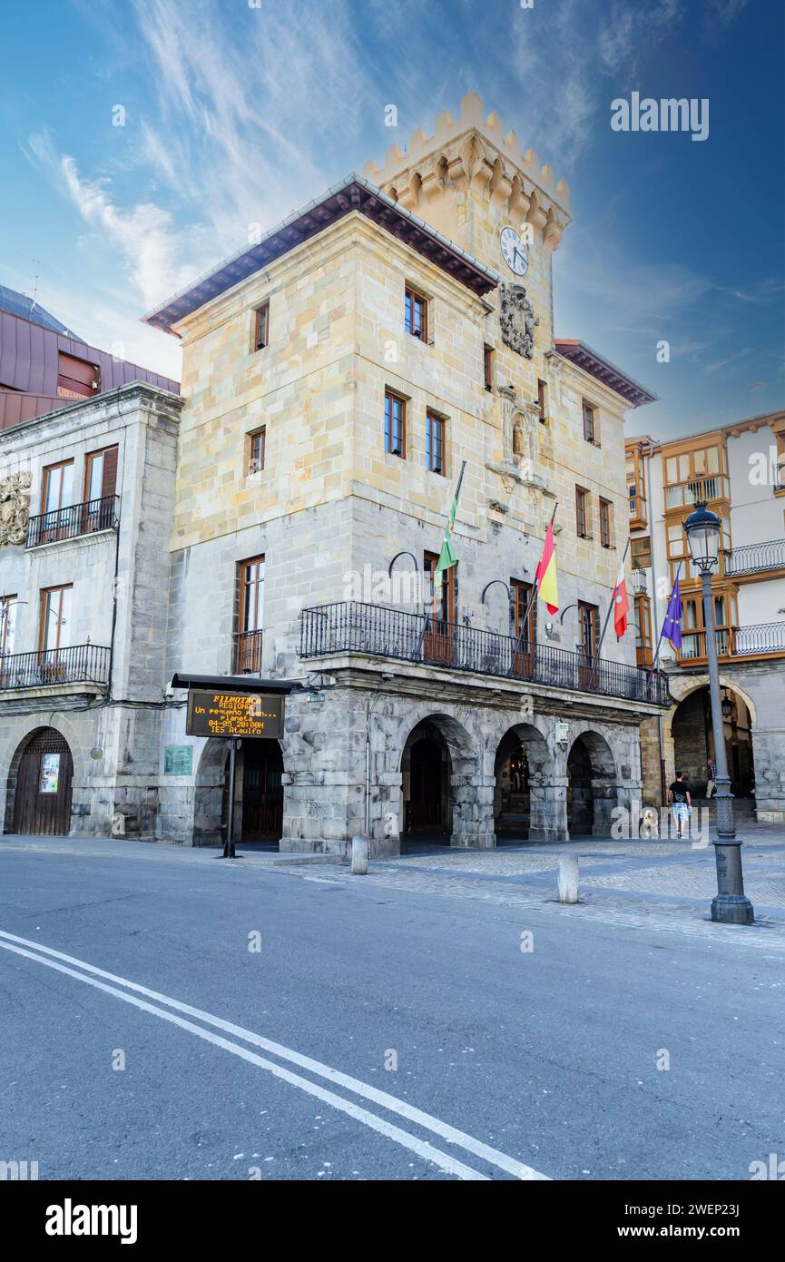 Un élégant hôtel de ville avec une tour de l'horloge, avec des arches en pierre et des drapeaux, sous un ciel bleu rusé Banque D'Images
