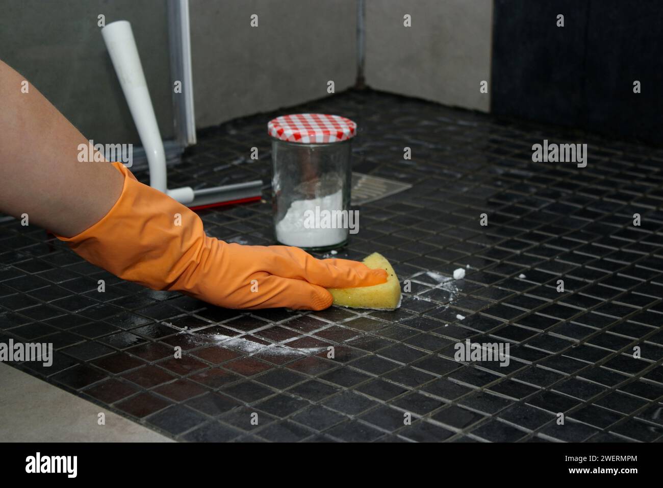 Gros plan des mains de la femme dans des gants orange nettoyant le sol de la douche avec du bicarbonate de soude, concept de nettoyage respectueux de l'environnement Banque D'Images
