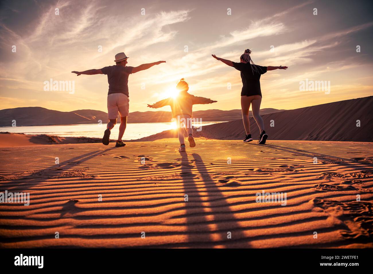Heureuse jeune famille avec le père, la mère et la petite fille s'amusent et courent dans les dunes de coucher du soleil et le lac désert en oasis Banque D'Images