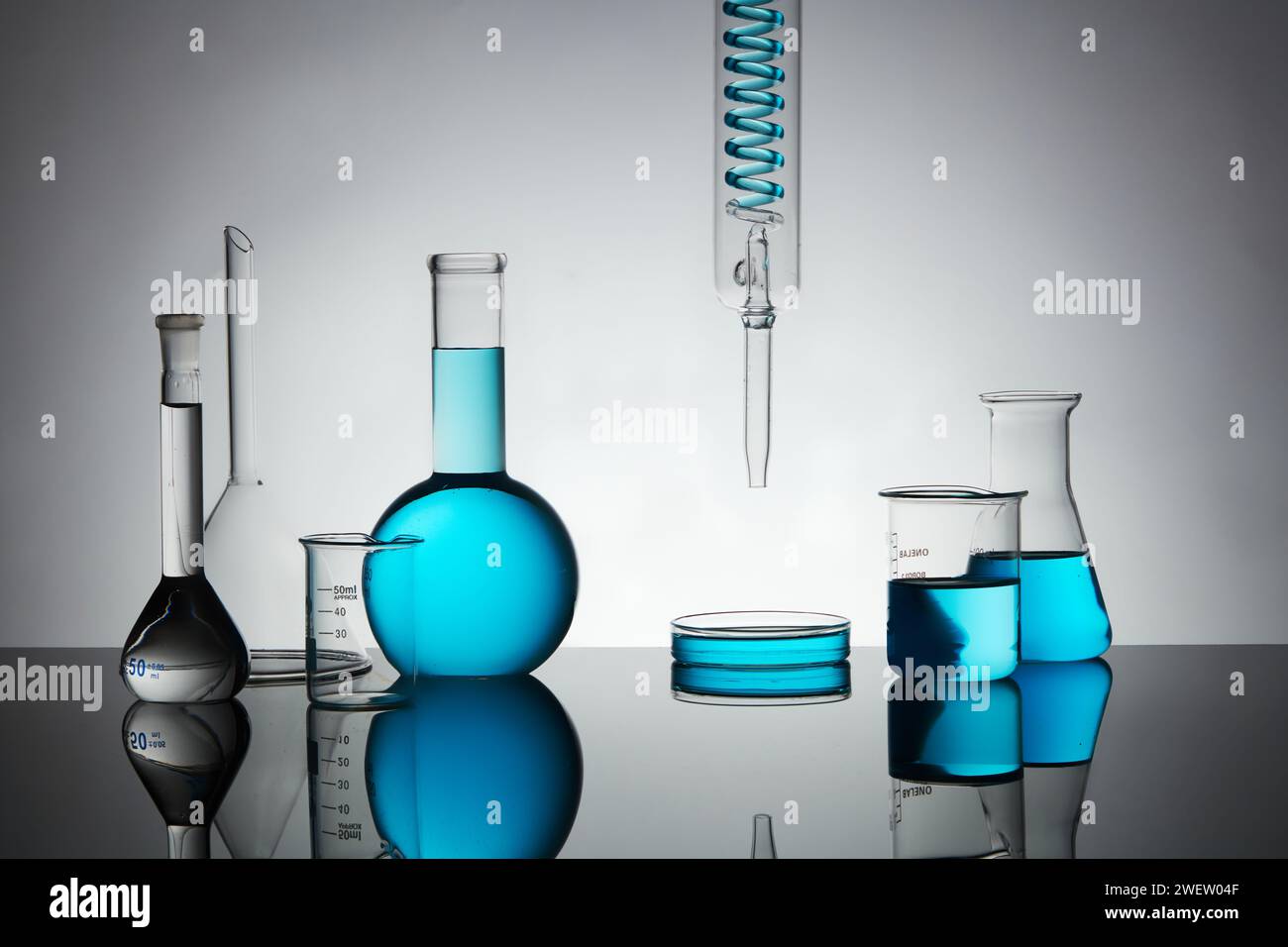 Fond minimal art avec boîte de Pétri, bécher, flacon erlenmeyer, flacon bouillant et verrerie de laboratoire contenant du liquide bleu sur fond rétro-éclairé. Banque D'Images