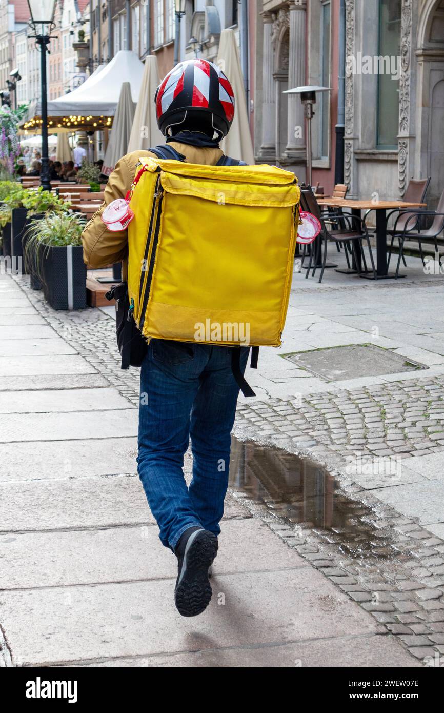 Un motocycliste avec un sac à dos jaune et un casque marche le long du trottoir de pierre Banque D'Images