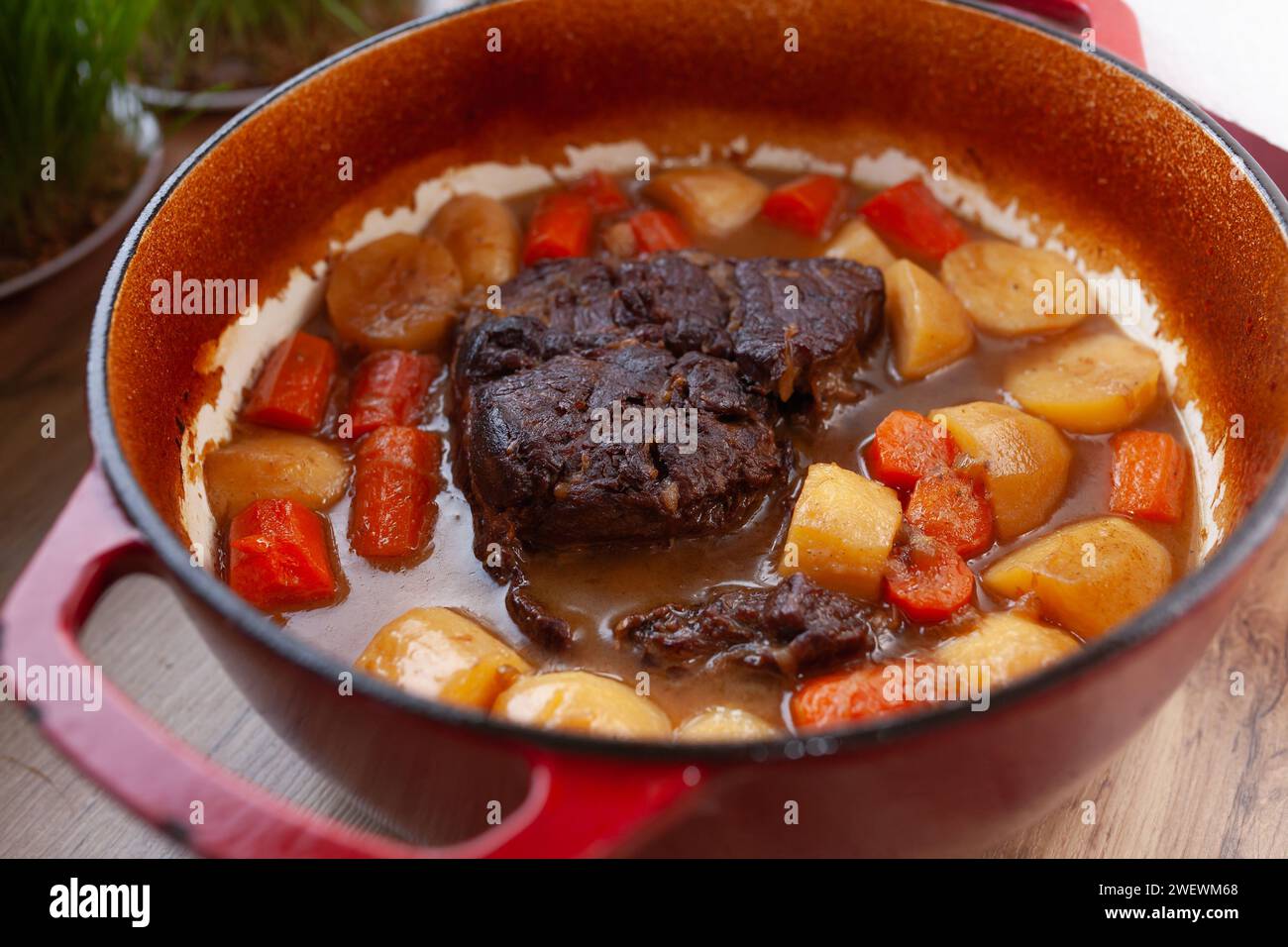 Rôti en cocotte avec carottes et pommes de terre cuites lentement dans un four hollandais rouge, sur la table de la cuisine Banque D'Images