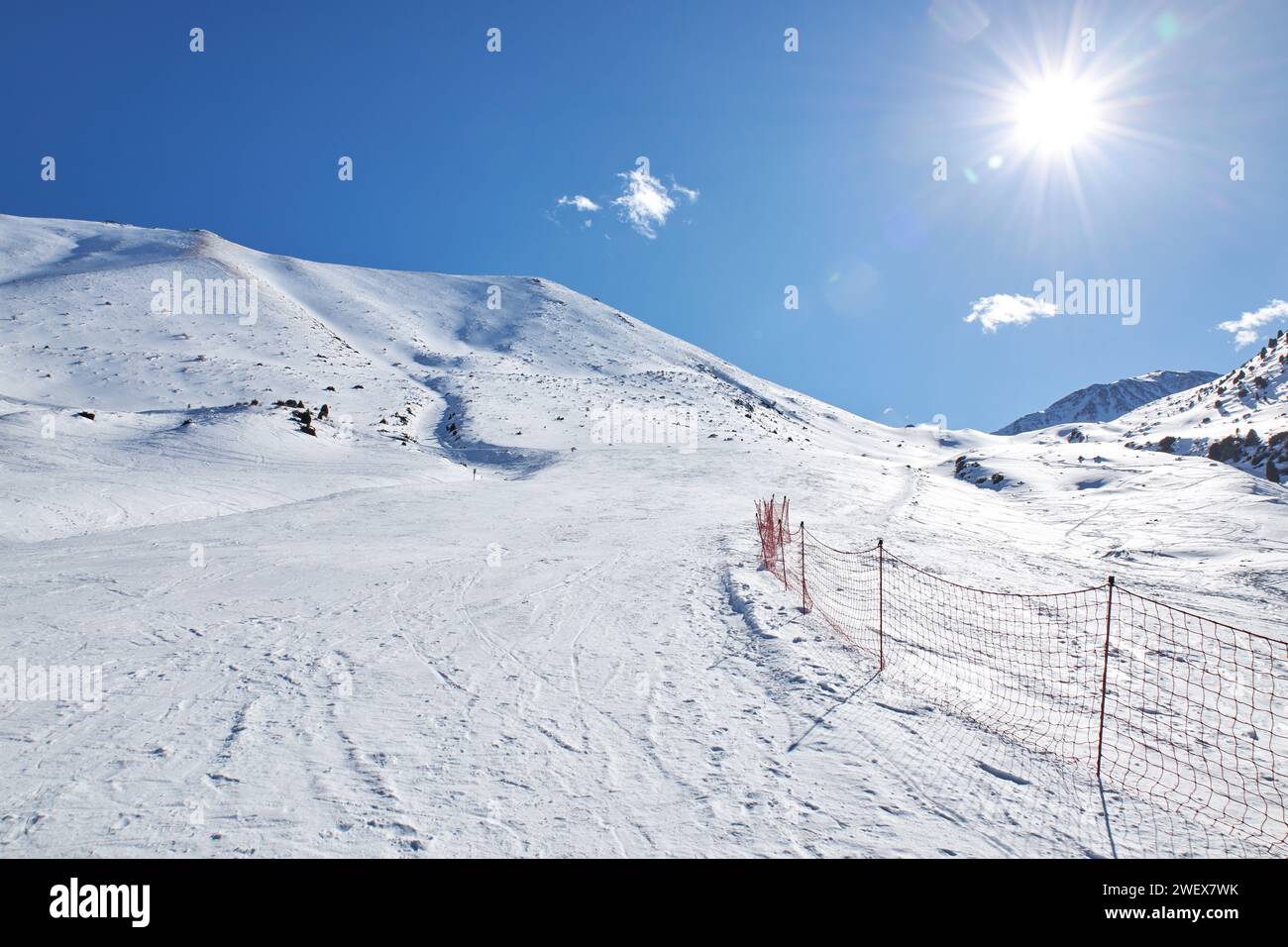 Piste vide à la station de ski, piste de montagne. Clôture en maille rouge marquant la zone dangereuse et la frontière de la route. Paysage de montagnes d'hiver au soleil Banque D'Images
